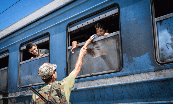 Një polic maqedonas përshendet refugjatët në tren. 25 gusht 2015. Foto nga Elvin Shulku